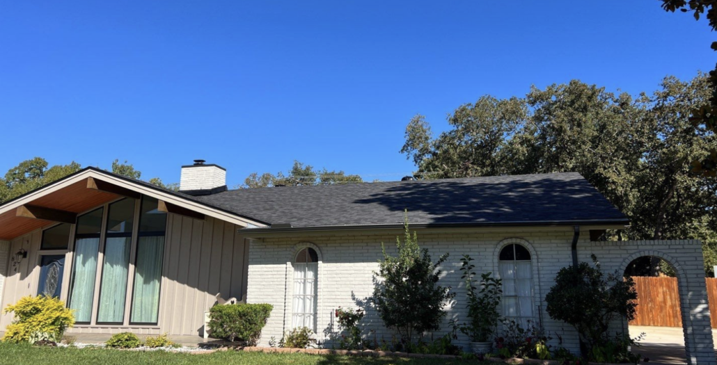brand new roof on home with bright blue sky with tree giving shad over the right side of the home. 